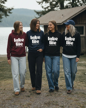 Four women walking and laughing together in lake life hoodies, with the blonde woman wearing a navy cap