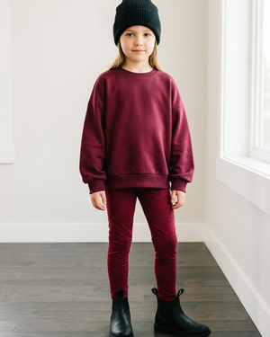 Full-body girl in a burgundy lounge sweater and small bow-pattern leggings, black Chelsea boots, and a black beanie, with room for a 4:5 crop
