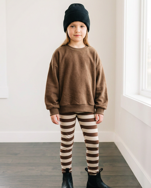 Girl in a brown lounge sweater and brown-and-cream stripe leggings, with extra white space for cropping