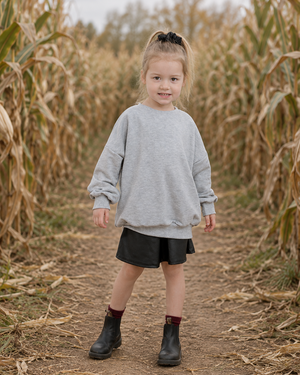 Girl in a grey sweatshirt and black skirt standing in a muted corn maze