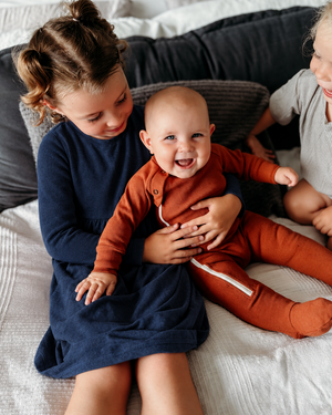 Girl wearing a navy long-sleeved dress while holding a baby