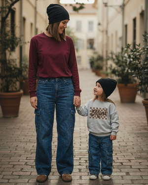 Mom and two-year-old daughter on a cobblestone lane, wearing beanies and wide-leg cargo jeans, with the daughter in the grey Mini sweater