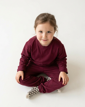 Overhead view of the girl in a matching burgundy top and sweatpants, with generous white space for a 4:5 crop