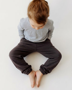 Overhead view of the girl’s charcoal sweatpants, showing their fit, seams and gathered ankles with extra space for a 4:5 crop