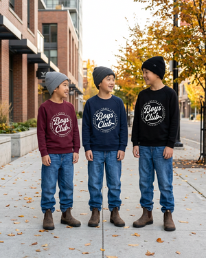 Three boys wearing navy, black, and burgundy Boys Club sweaters on a modern street in fall