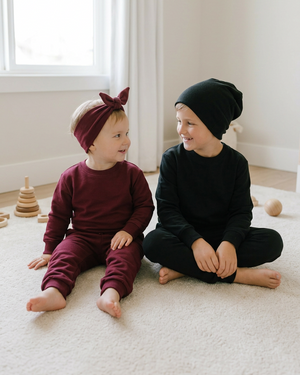 Toddler sitting beside a seven-year-old boy in a black crewneck, sweatpants, and beanie