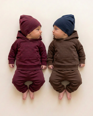 Two babies in burgundy and chocolate brown hoodie outfits with relaxed sweatpants matching the reference style